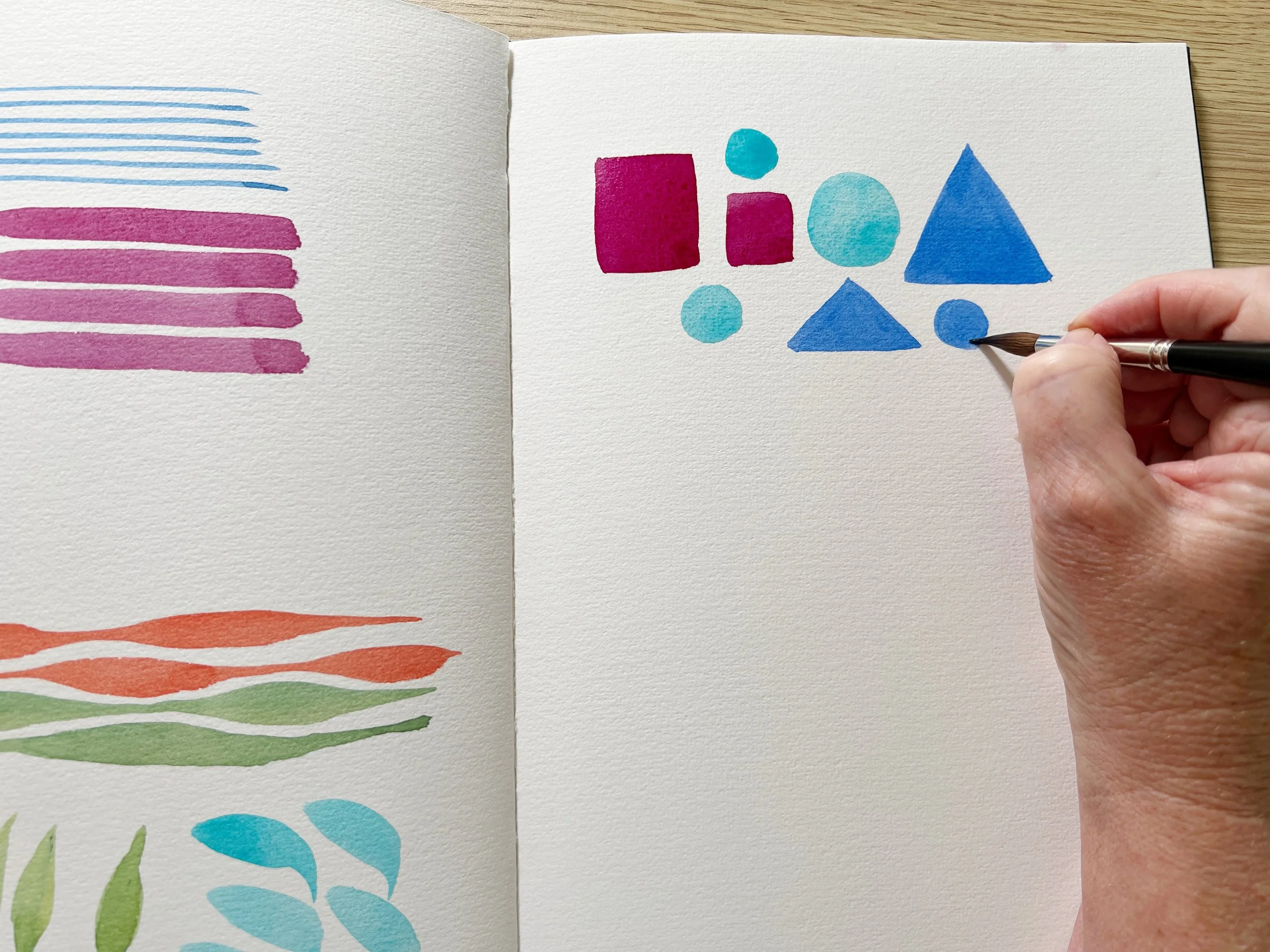 Practising brush control by painting colourful shapes in watercolour, including circles, squares, and triangles.
