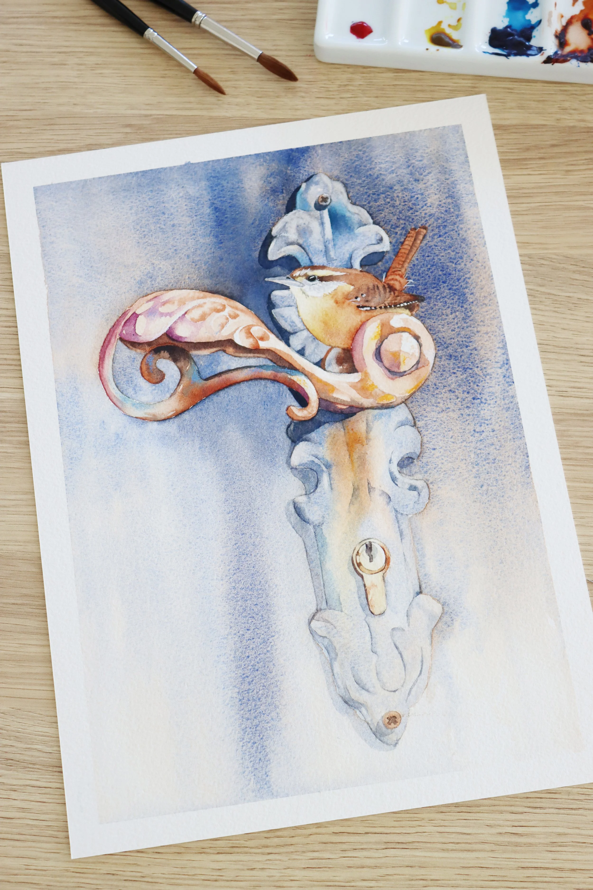 Watercolour painting of a small bird perched on an ornate blue door handle.