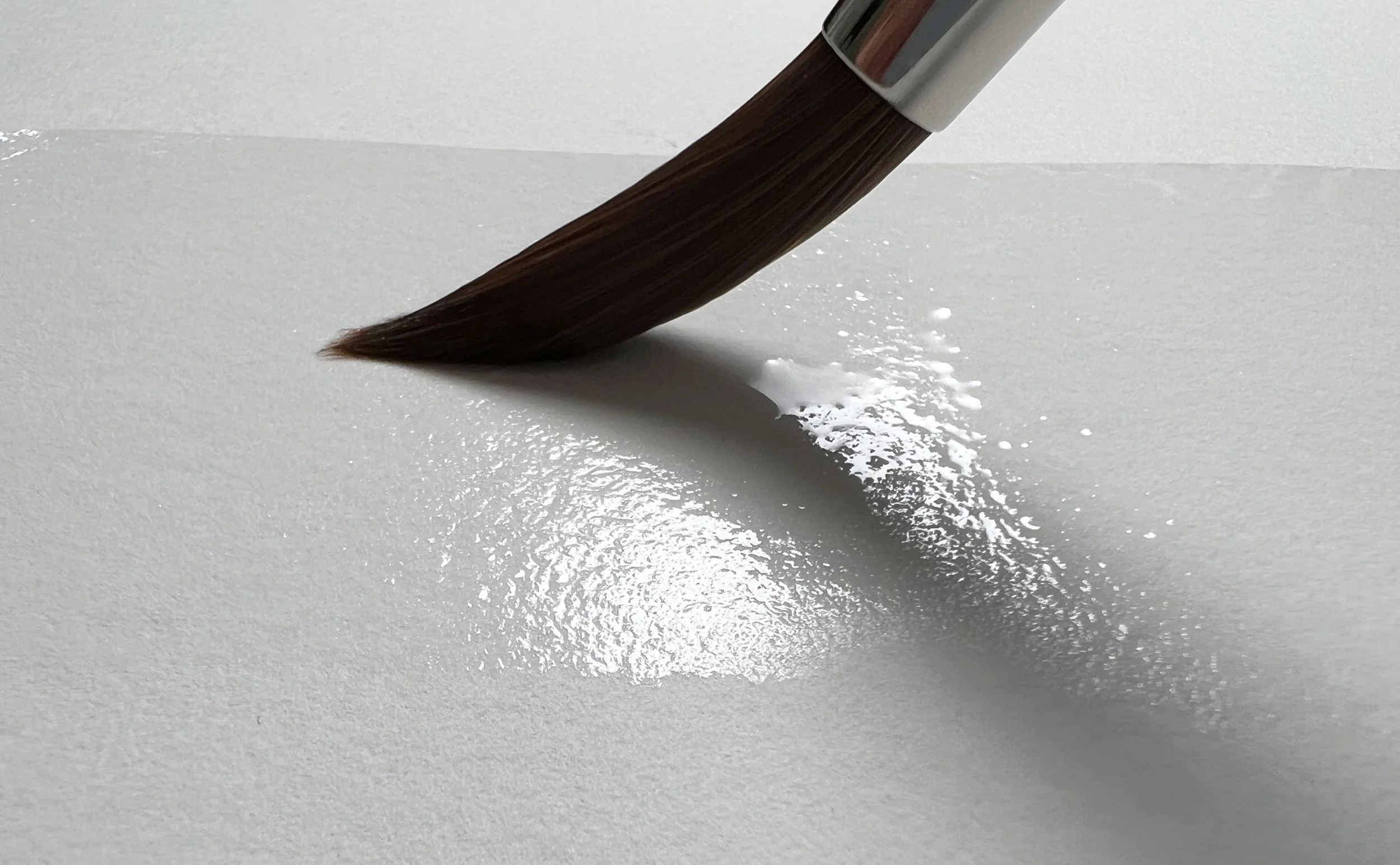 Large watercolour brush applying clean water to cold press paper in preparation for a wet-on-wet wash