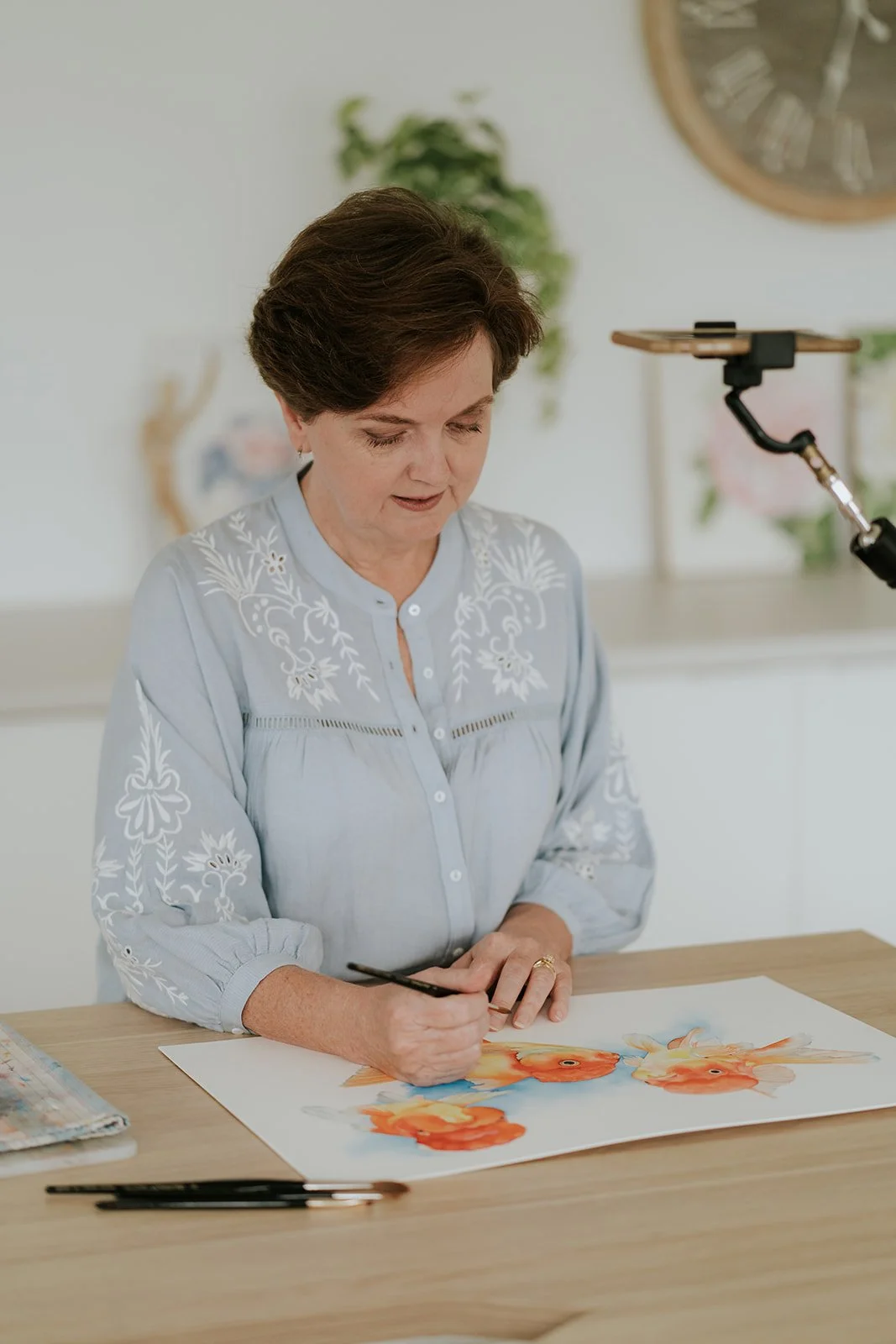 Artist Louise De Masi painting vibrant goldfish in watercolour at her desk, filmed for an online tutorial.