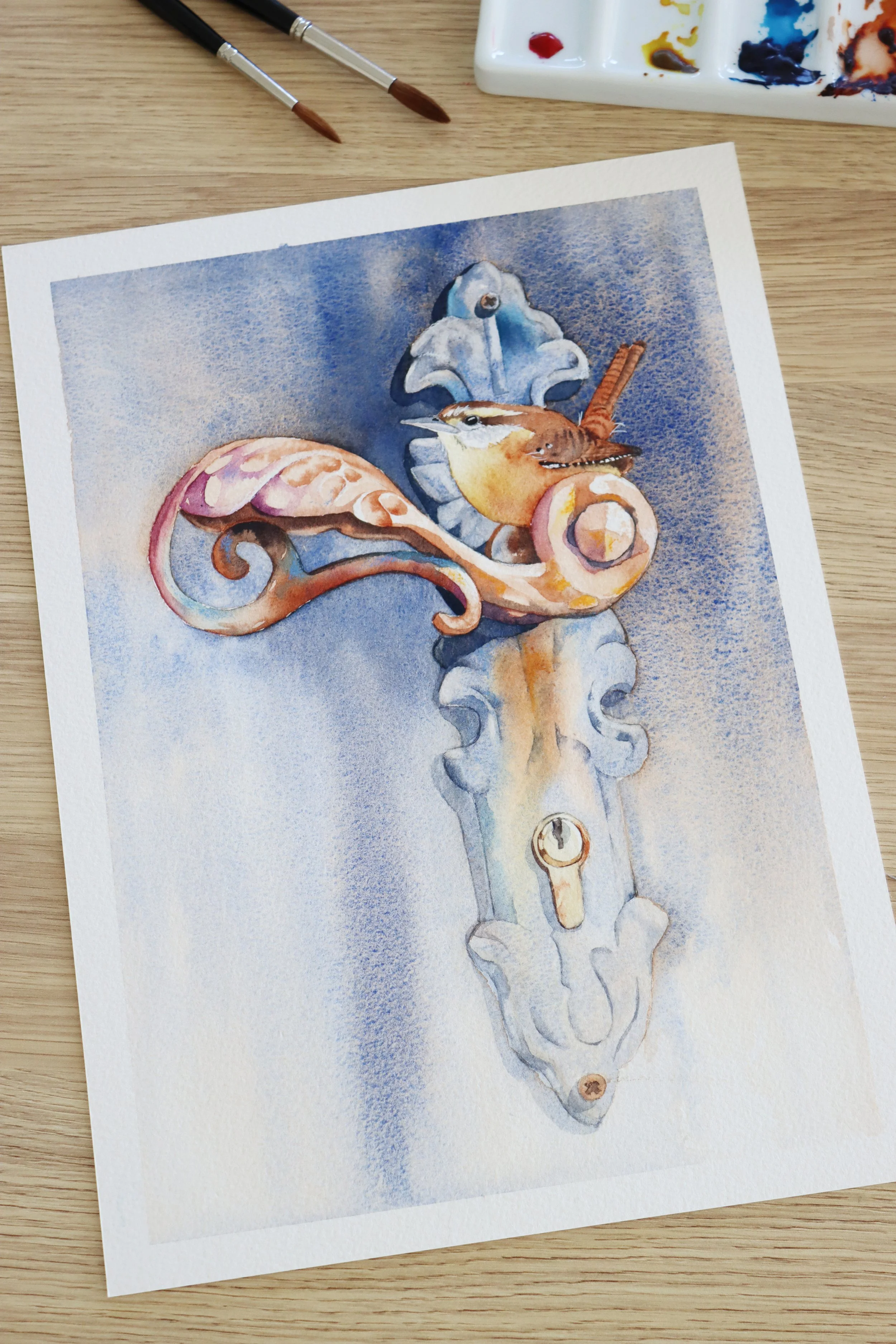 Watercolour painting by Louise De Masi of a small brown bird perched on an ornate vintage door handle against a blue textured background