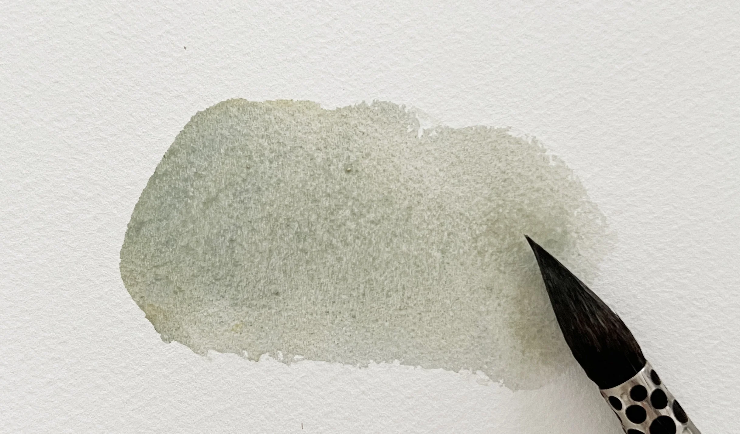 A watercolour mix swatch showing a soft, muted grey tone with visible granulation and brush texture.