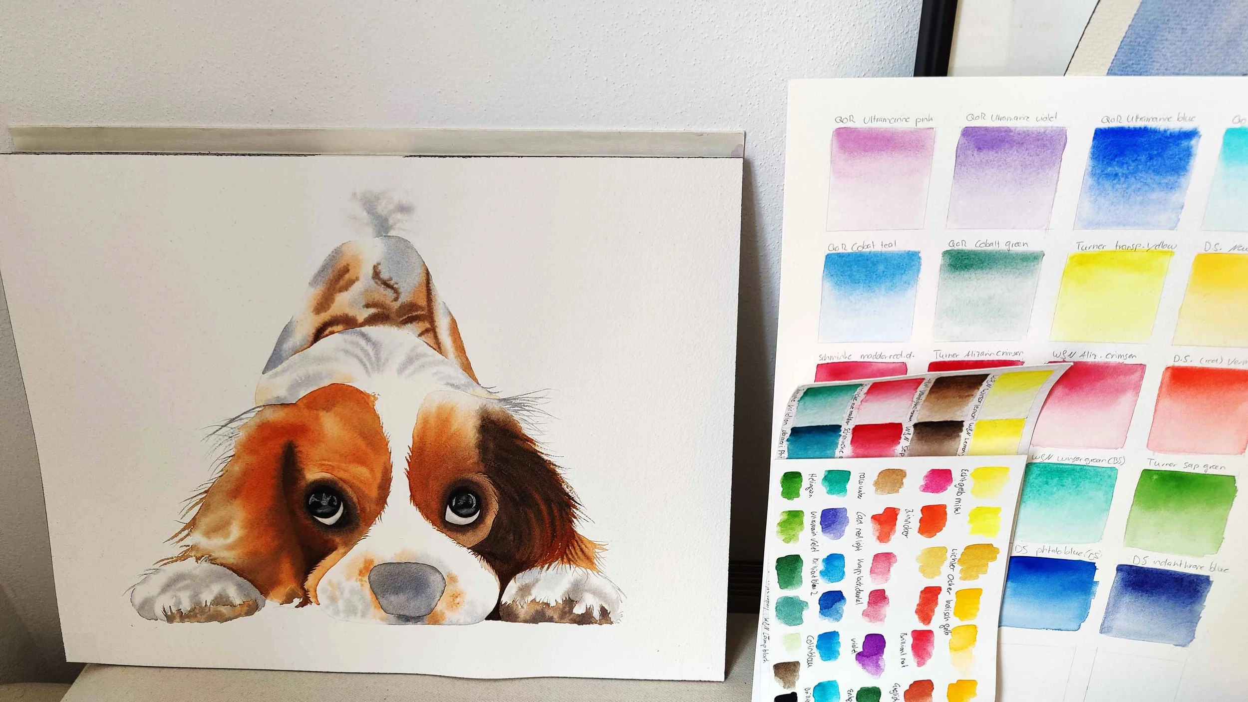 Realistic watercolour dog portrait beside a colour swatch chart showing various paint samples and gradients.