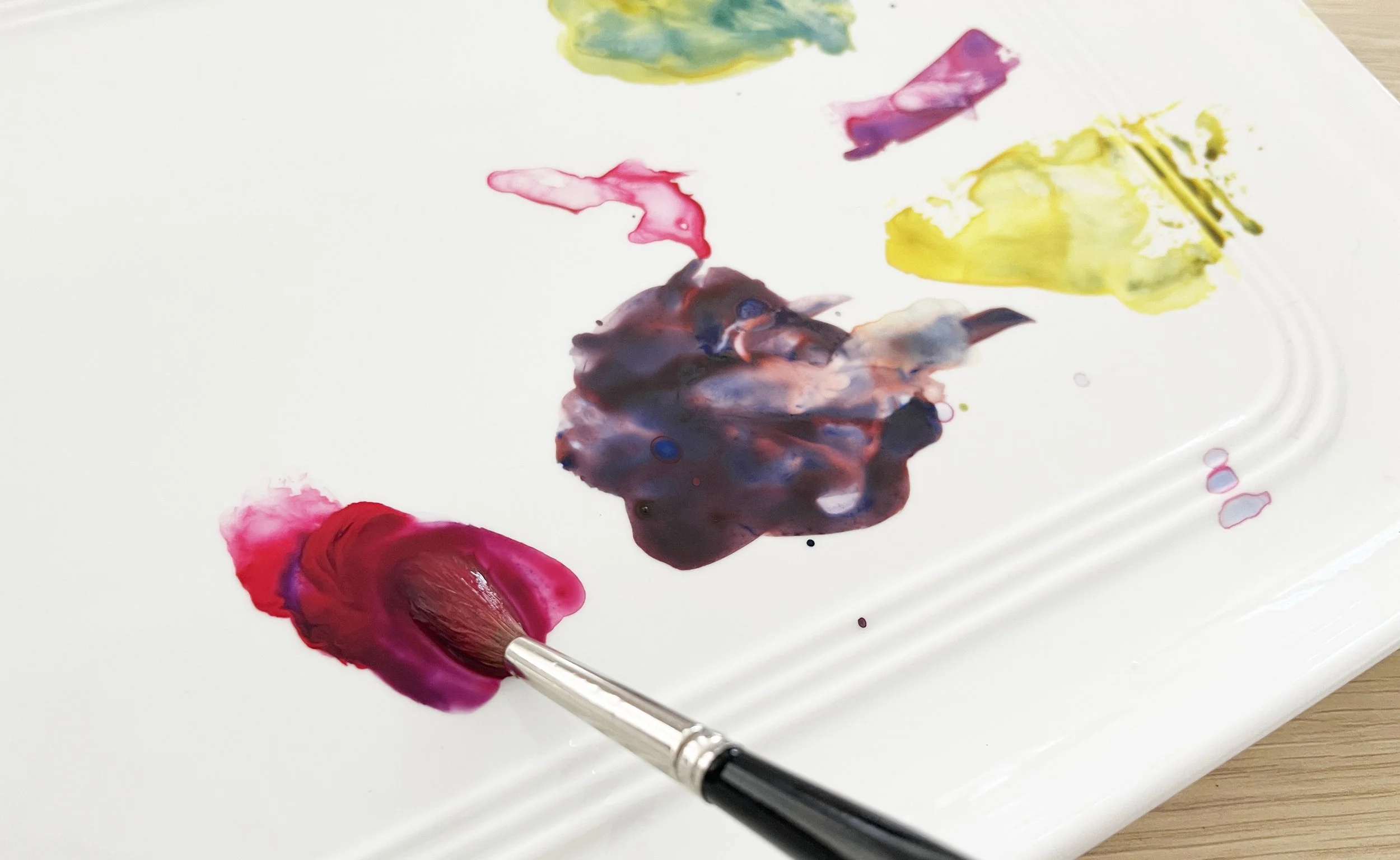 Watercolour paints being mixed on a white palette with a brush before painting.