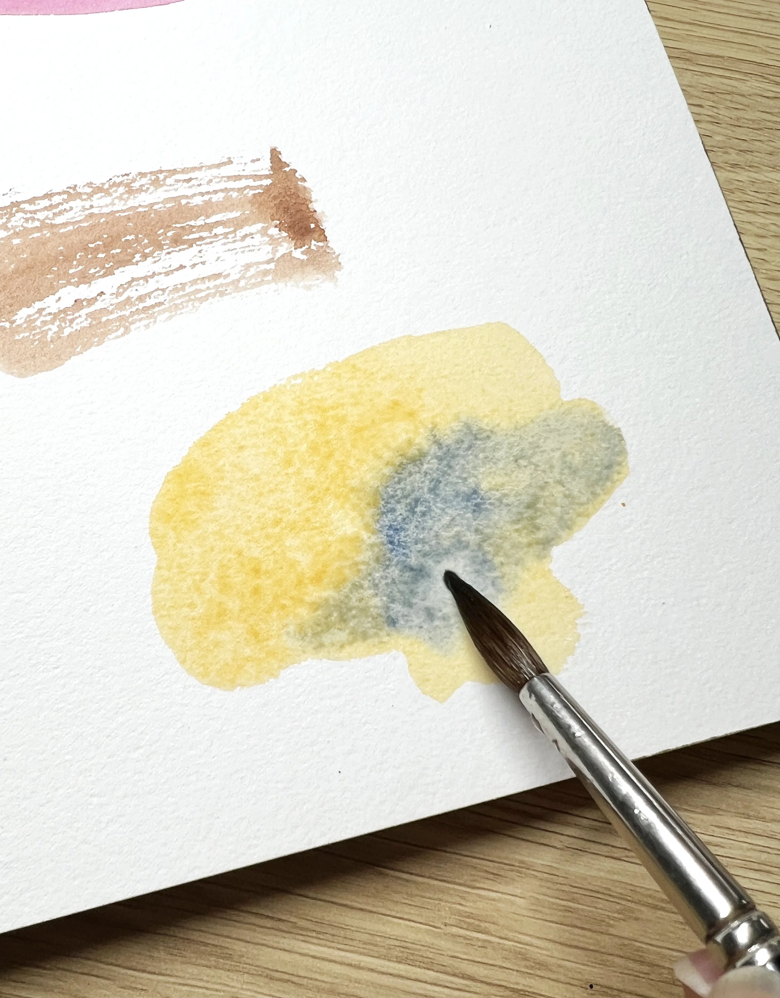 Watercolour charging technique with blue pigment dropped into a wet yellow wash to create natural blending effects.