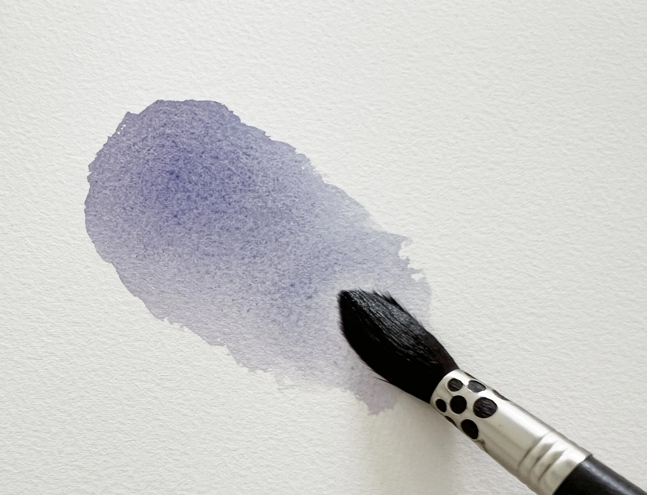 A brush blending French Ultramarine and Scarlet Lake watercolour paint into a soft granulating purple wash on paper.