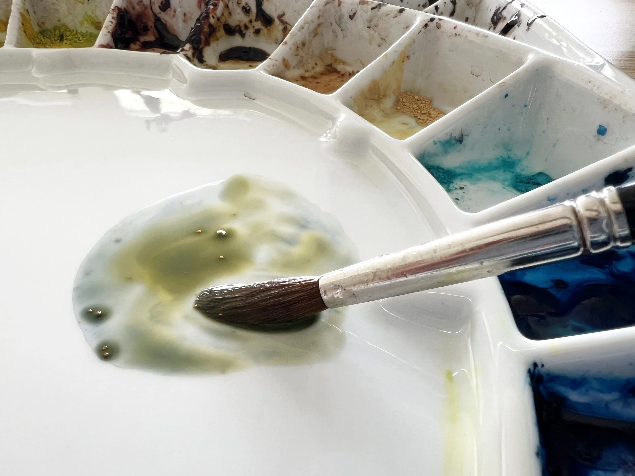 Close up of round brush blending a neutral green grey wash on a ceramic watercolour palette.