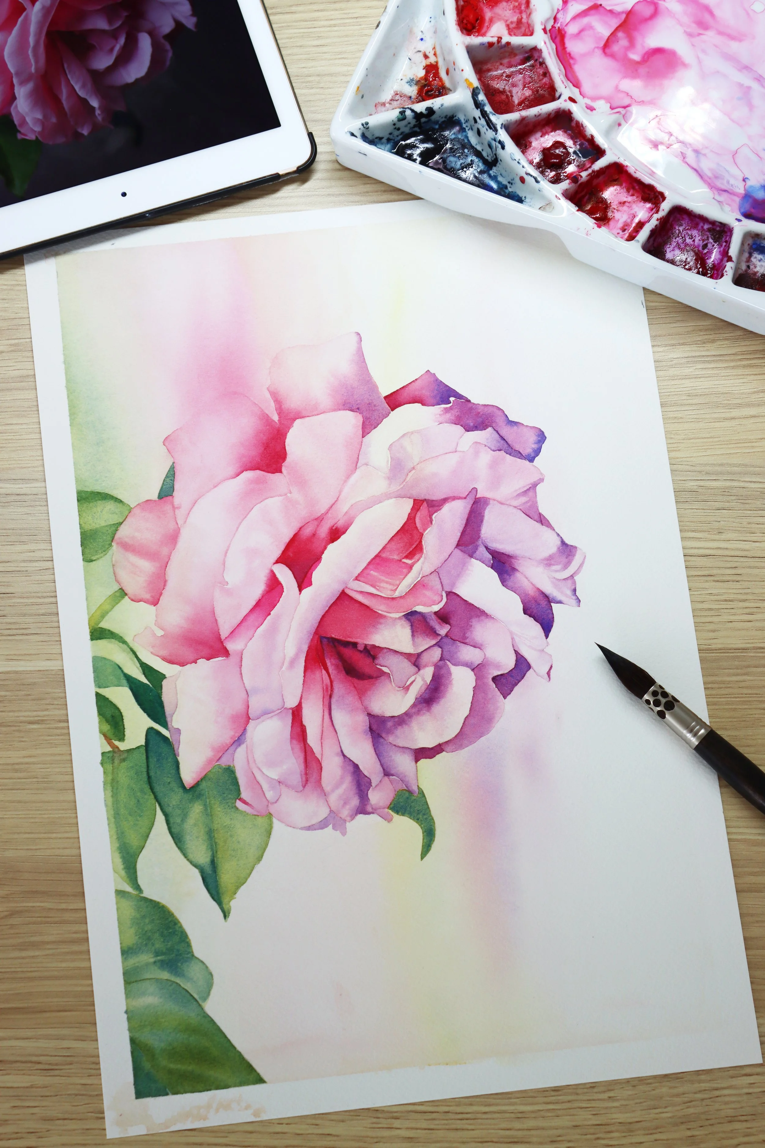 Watercolour rose painting with vibrant pink and purple petals, palette and reference photo visible nearby.