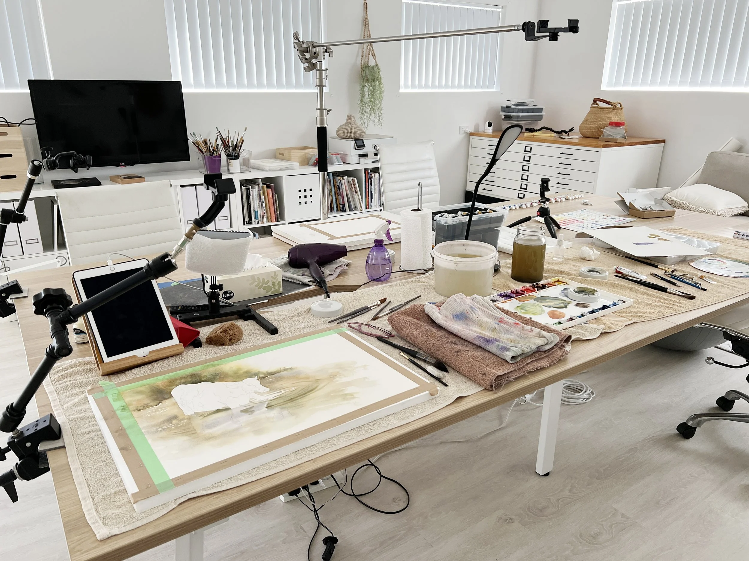 Overhead view of Louise’s studio setup with multiple cameras, iPads, paints and tools laid out for filming a watercolour tutorial.