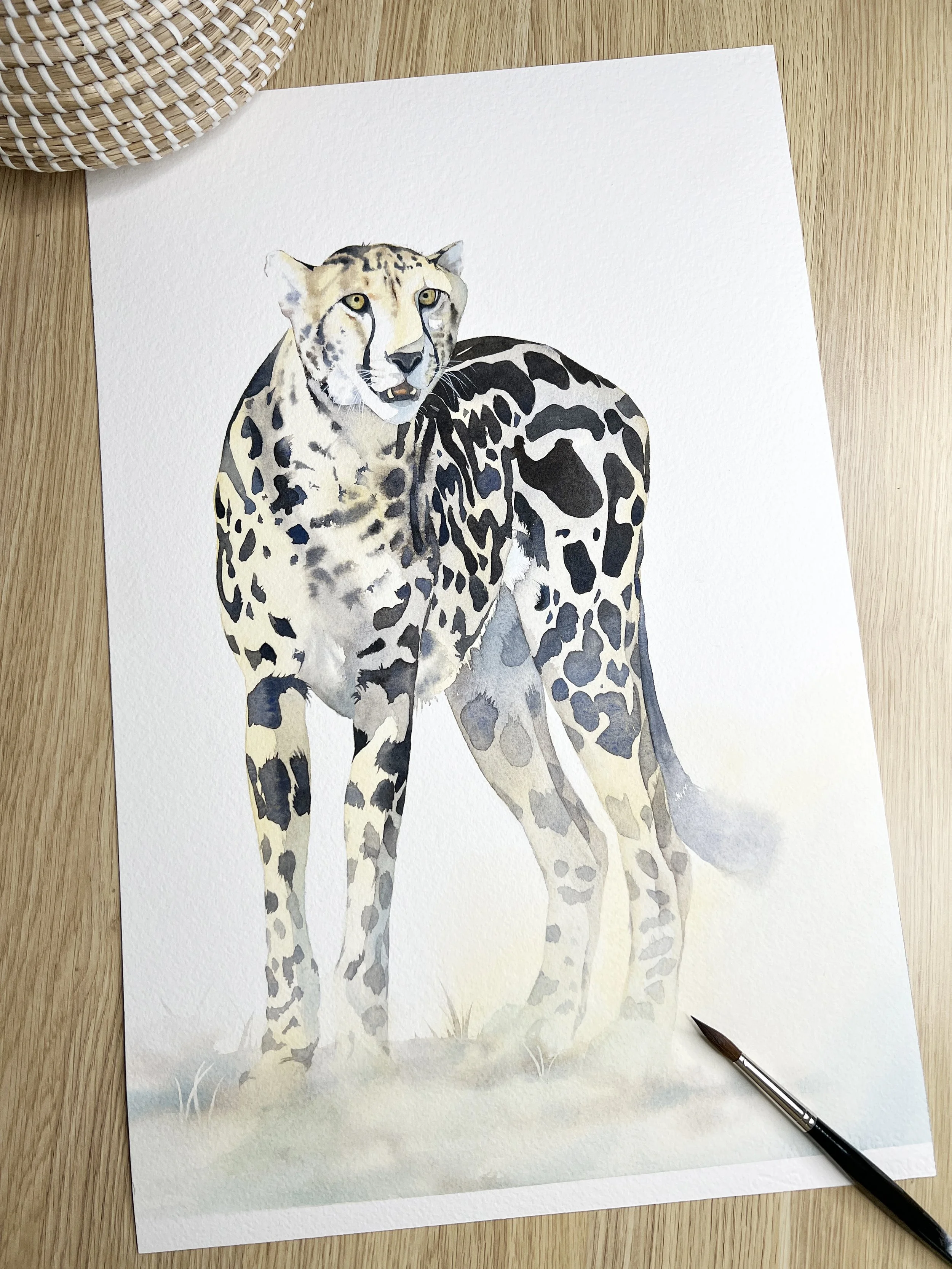Watercolour painting of a cheetah standing on soft grass, showing layered fur texture and controlled negative space on white paper.