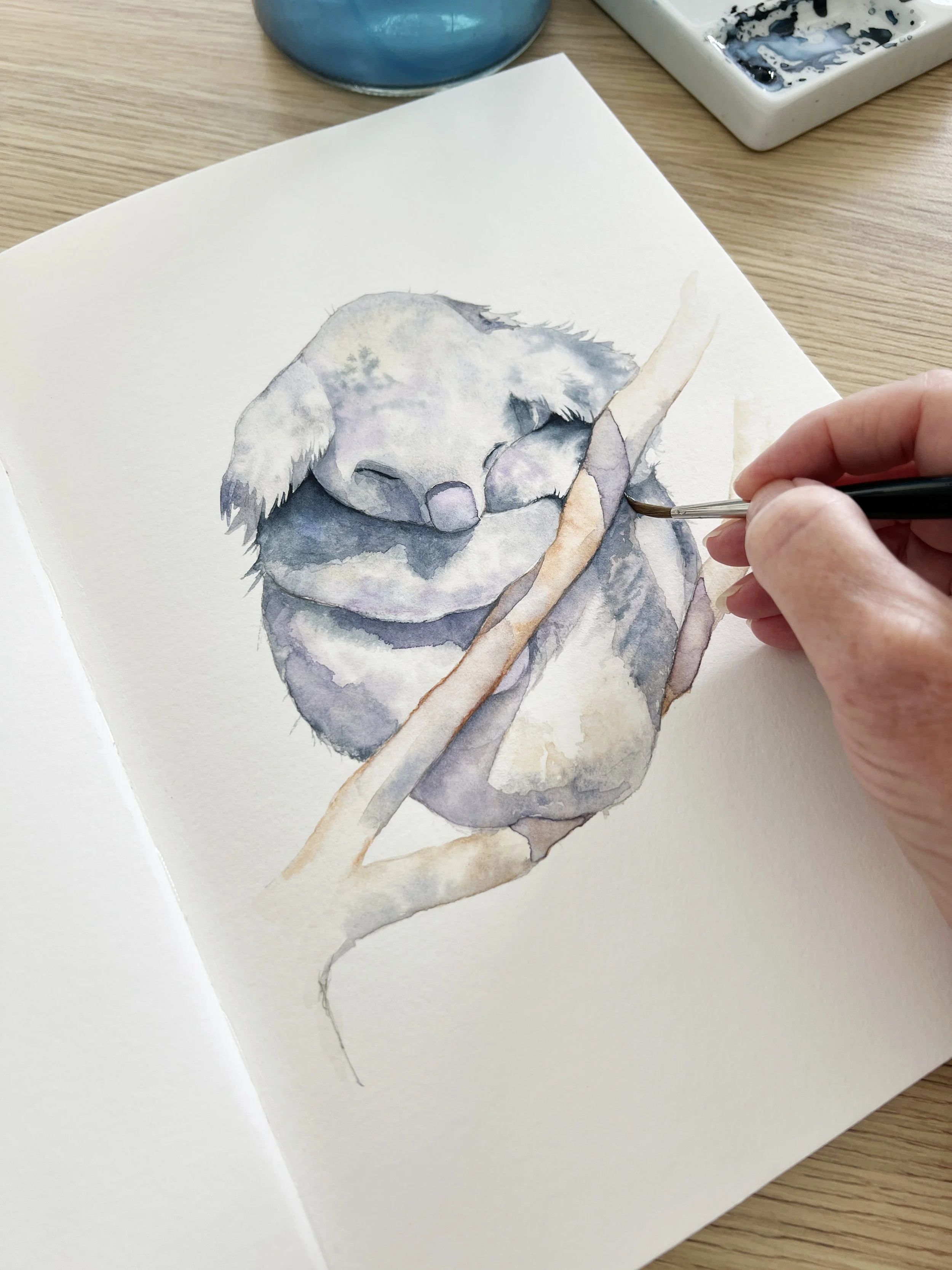 Hand painting a small owl perched on a branch using layered watercolour washes.
