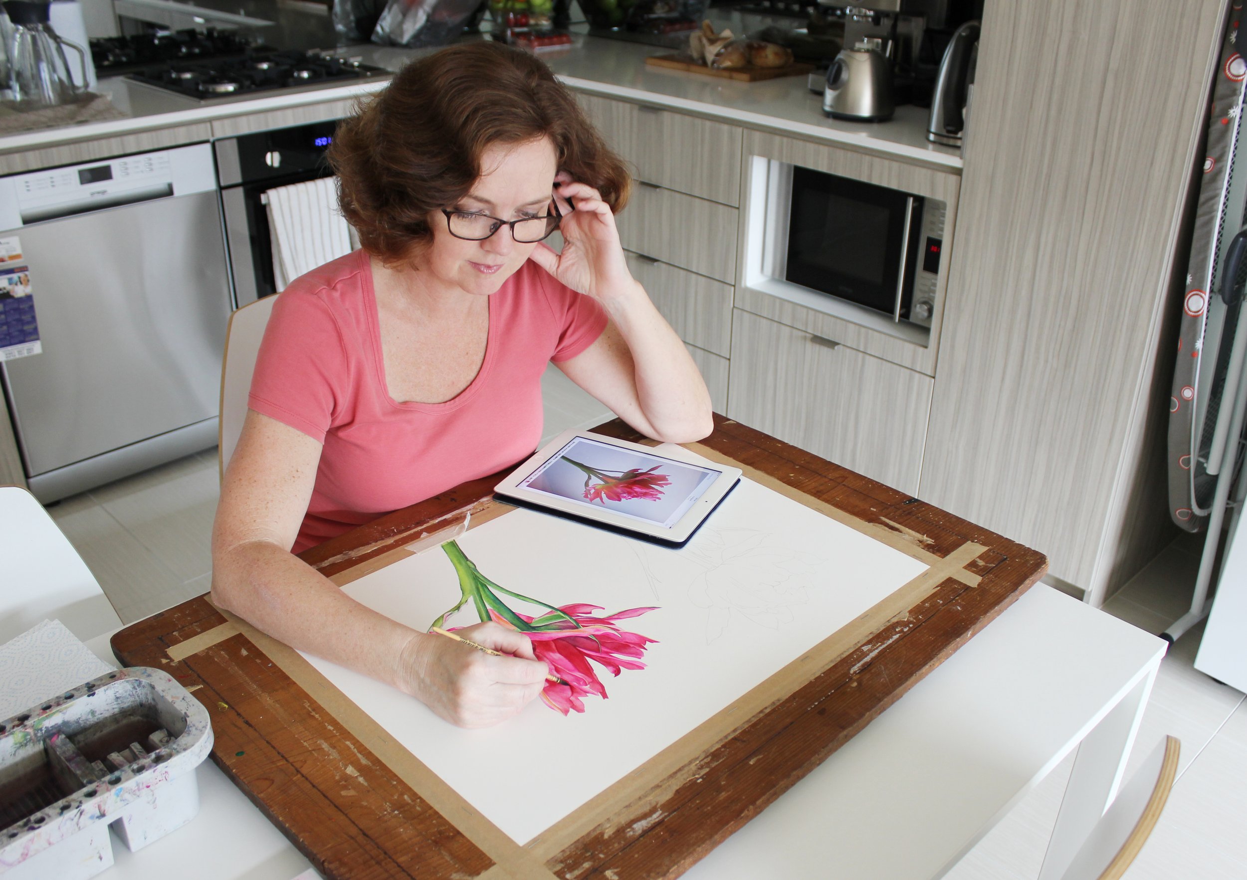Watercolour artist (Louise De Masi) painting a large pink flower while working from a reference photograph on a tablet.