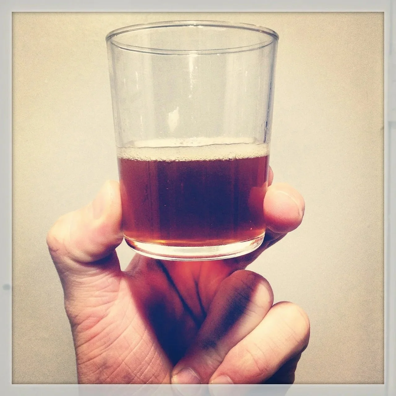 White hand holding small glass of brown beer