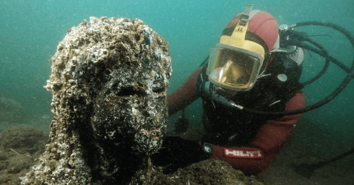 Diver underwater with barnacle covered statue head