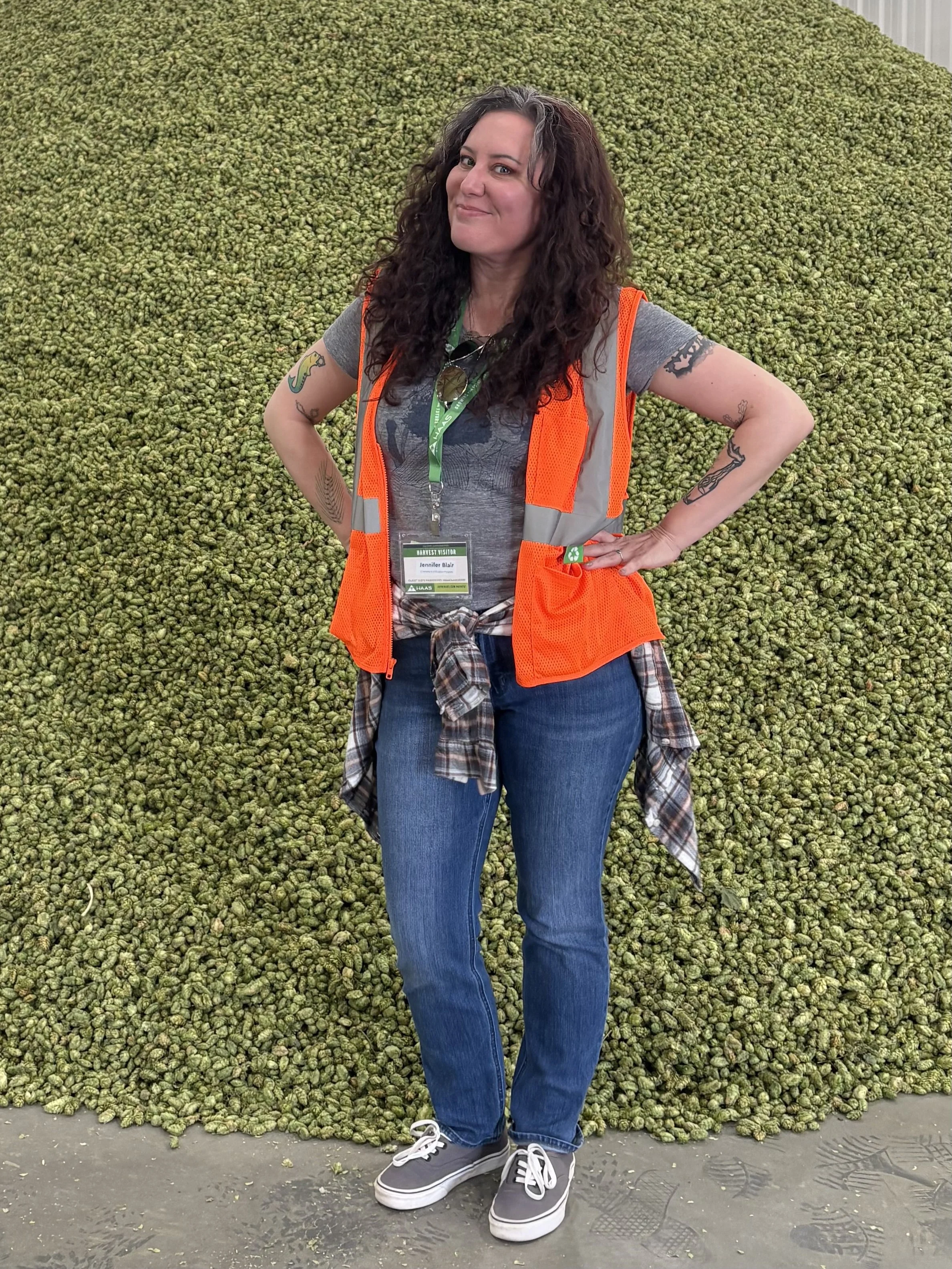 Jen Blair in orange safety vest standing in front of pile of hops