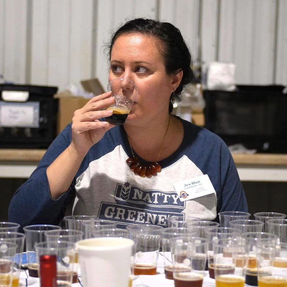 Jen Blair drinking dark beer with several beer samples on table