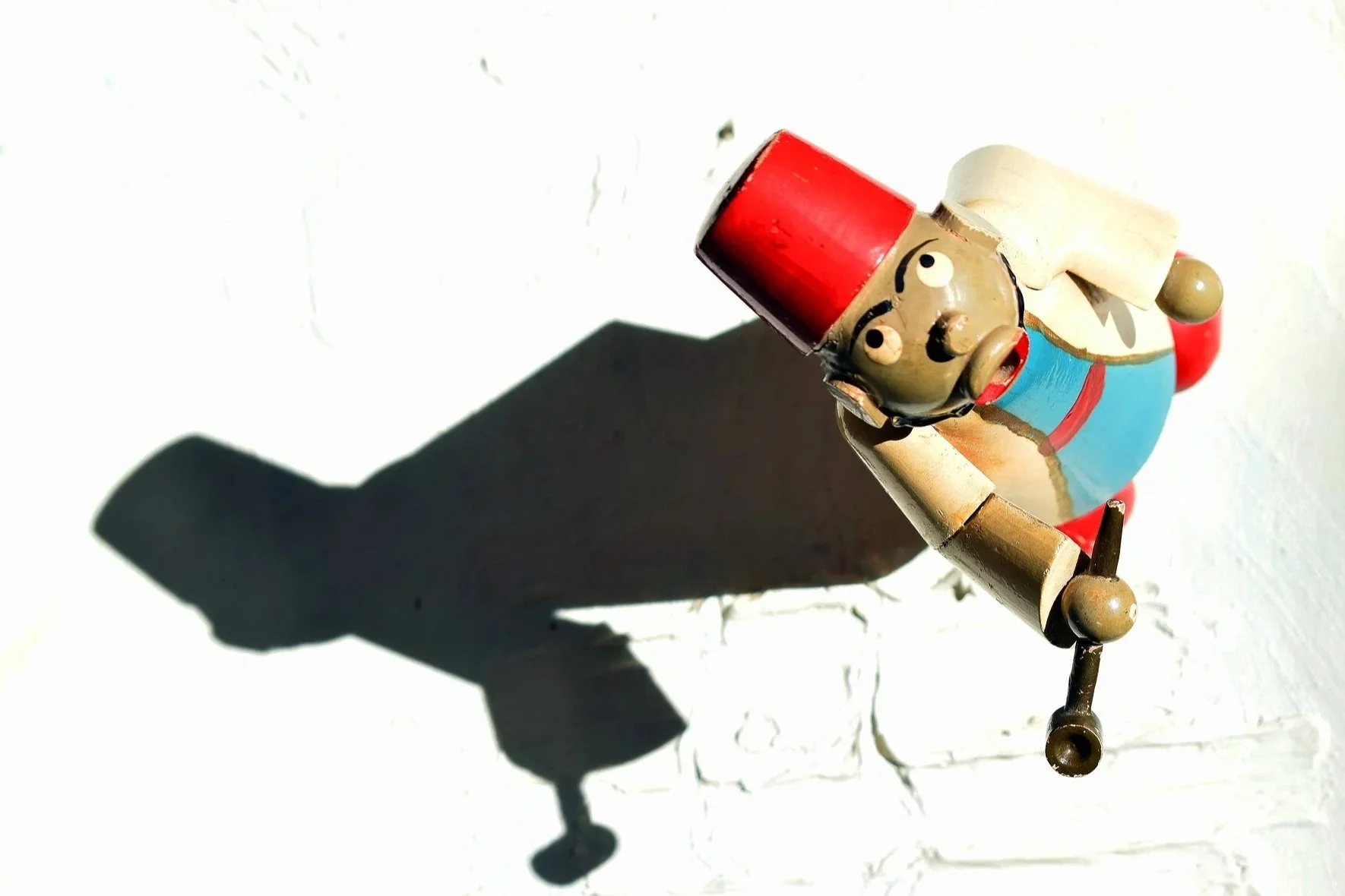Wooden toy man with red fez and sad face casting a black shadow on a whote background