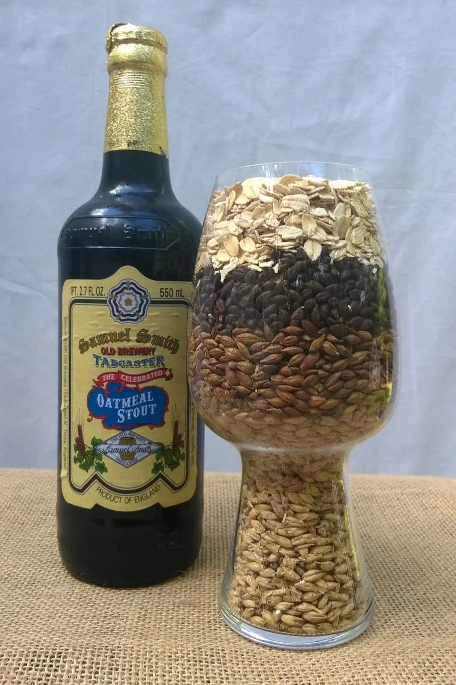 Samuel Smith Oatmeal Stout bottle next to stout glass filled with malted barley, roasted barley, and oatmeal