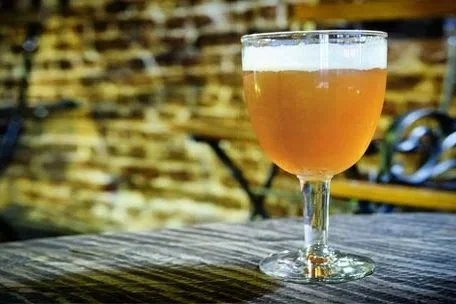 Belgian Tripel in goblet on wooden table with brick wall in background