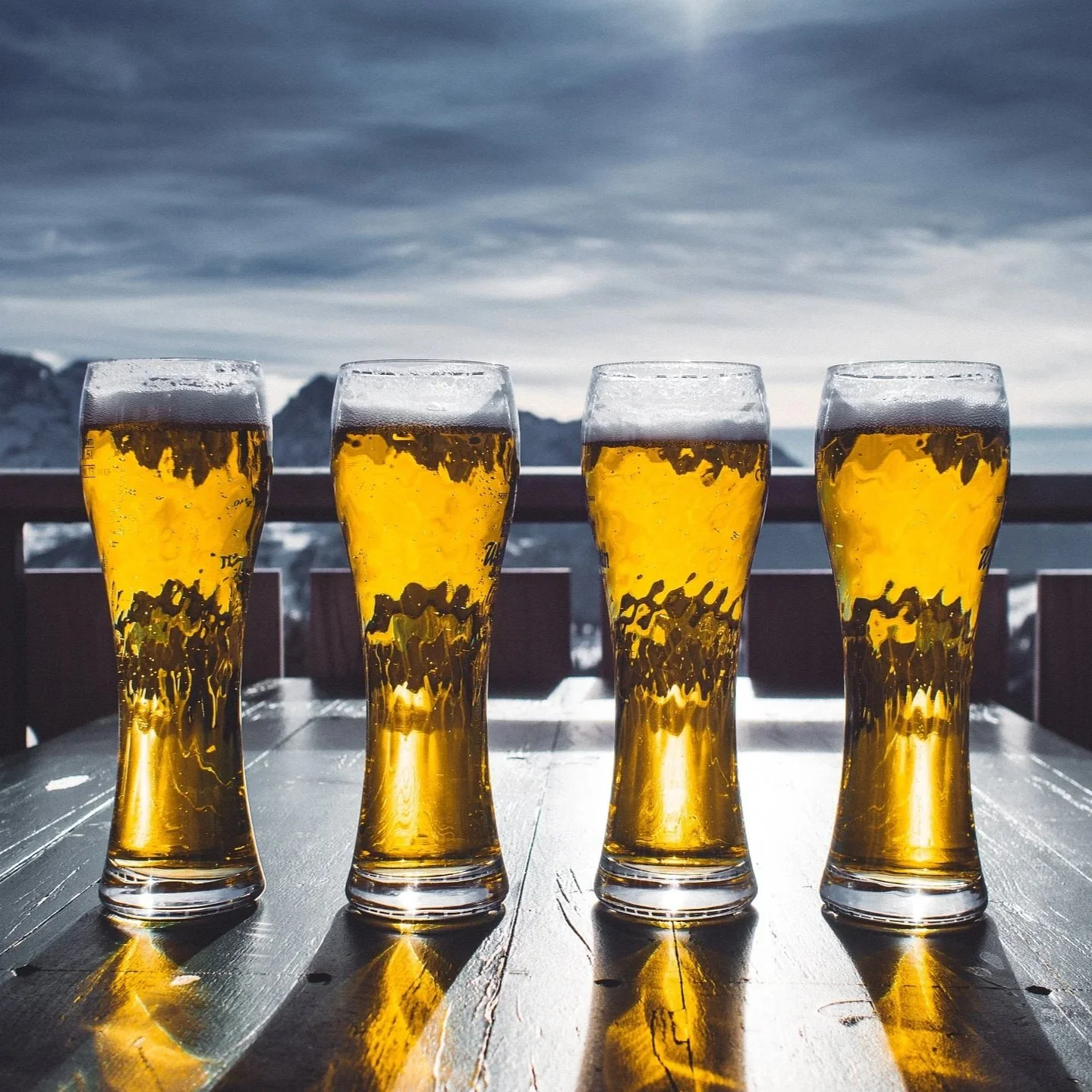 Four glasses of pale beer on a table with mountain background