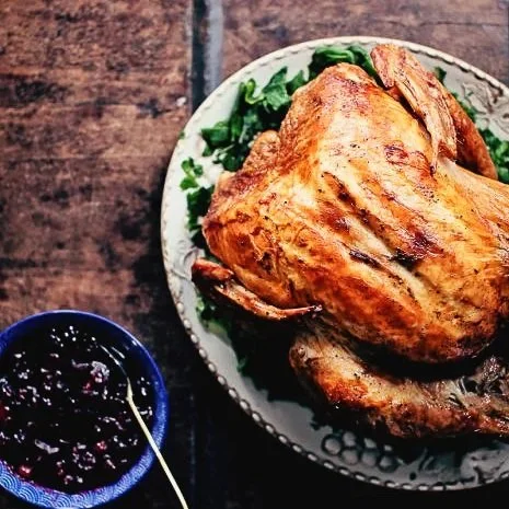 Roasted turkey on white plate next to blue bowl of cranberry sauce on wooden table