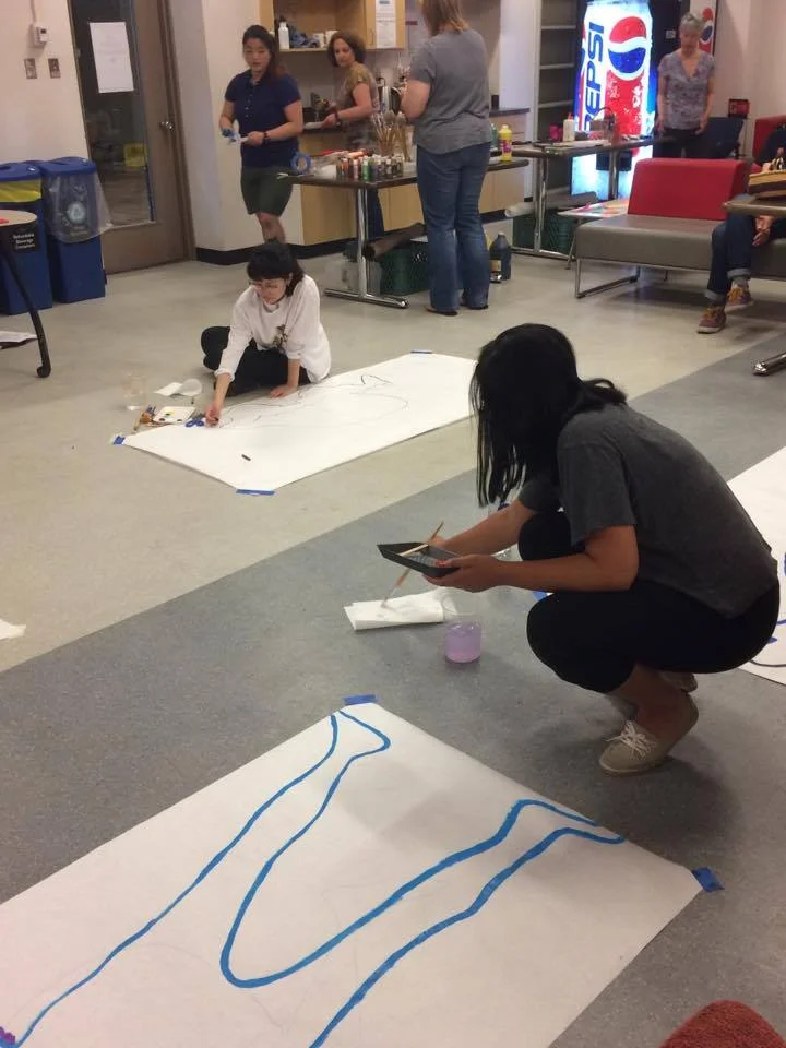 Participants started off by tracing their outlines in a variety of positions.Image description: two people with large sheets of white paper trace their outlines in paint and crayon.