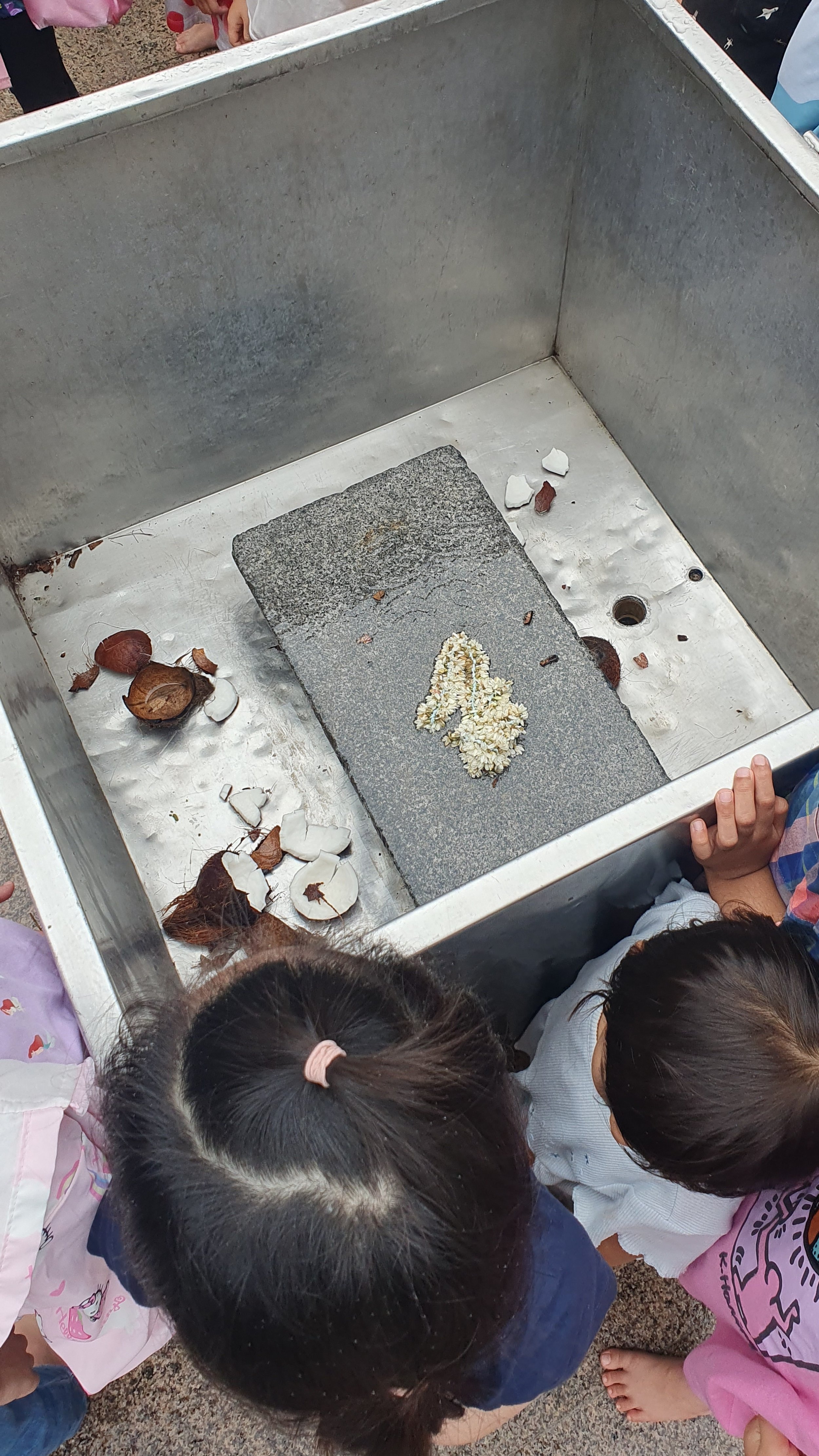  In this metal basin, there is a block of granite where worshippers smash a coconut as a prayer offering.   