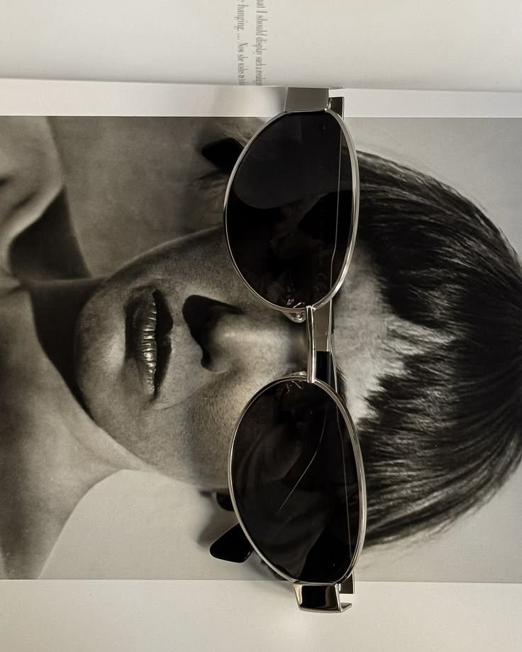 A pair of black sunglasses resting on a black-and-white photograph of a woman with short hair.