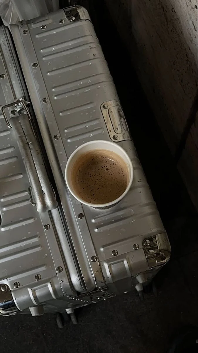A cup of coffee resting on a metal hard-shell suitcase.