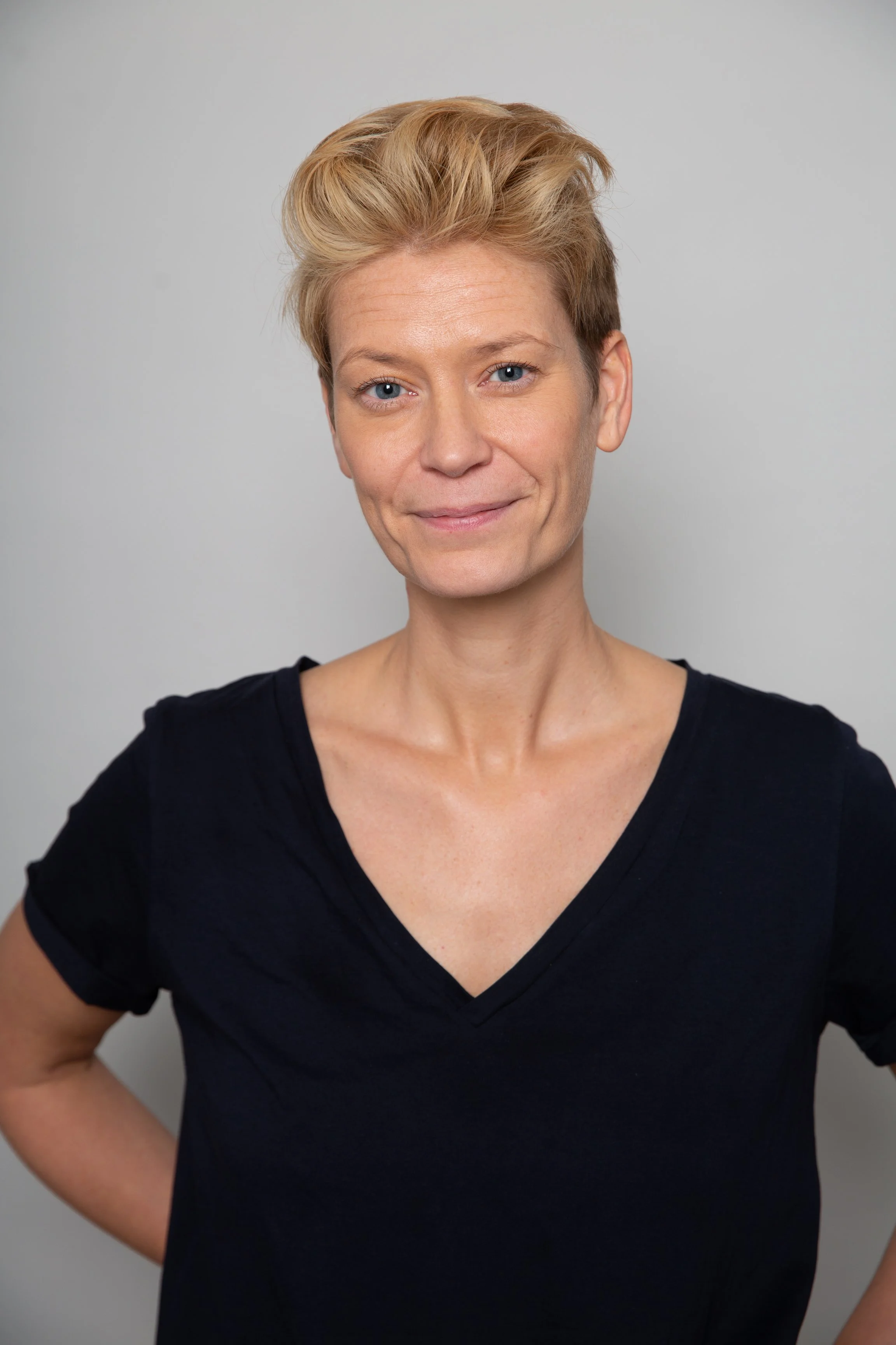 Headshot of Gem Barton, standing against a neutral grey background, looking into the camera.