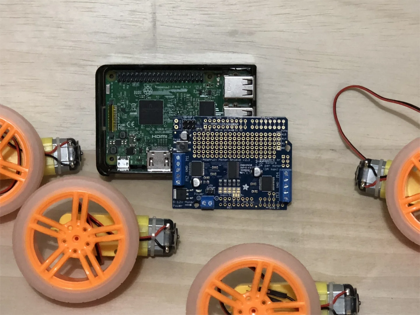 The Raspberry Pi (center-back), Pi Hat from Adafruit (center-front), wheels and TT motors. Batteries not included.