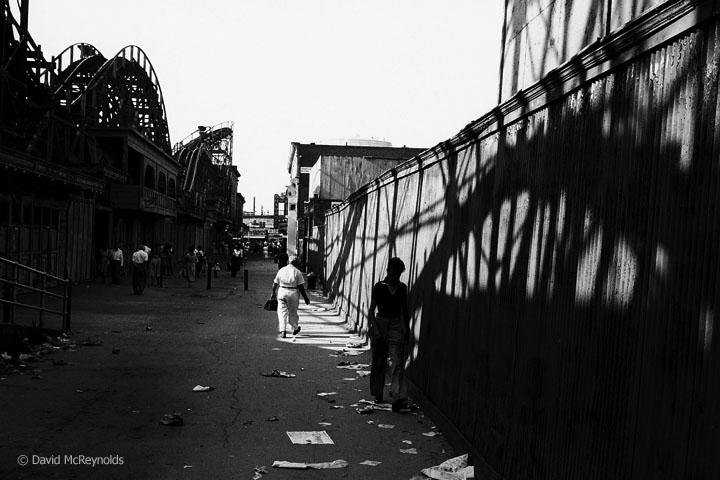 Coney Island, 1957. Possibly the Tornado roller coaster. Sign for the Shamrock Irish House, a restaurant, cabaret, and bar is down the alley on the right. (57-17)