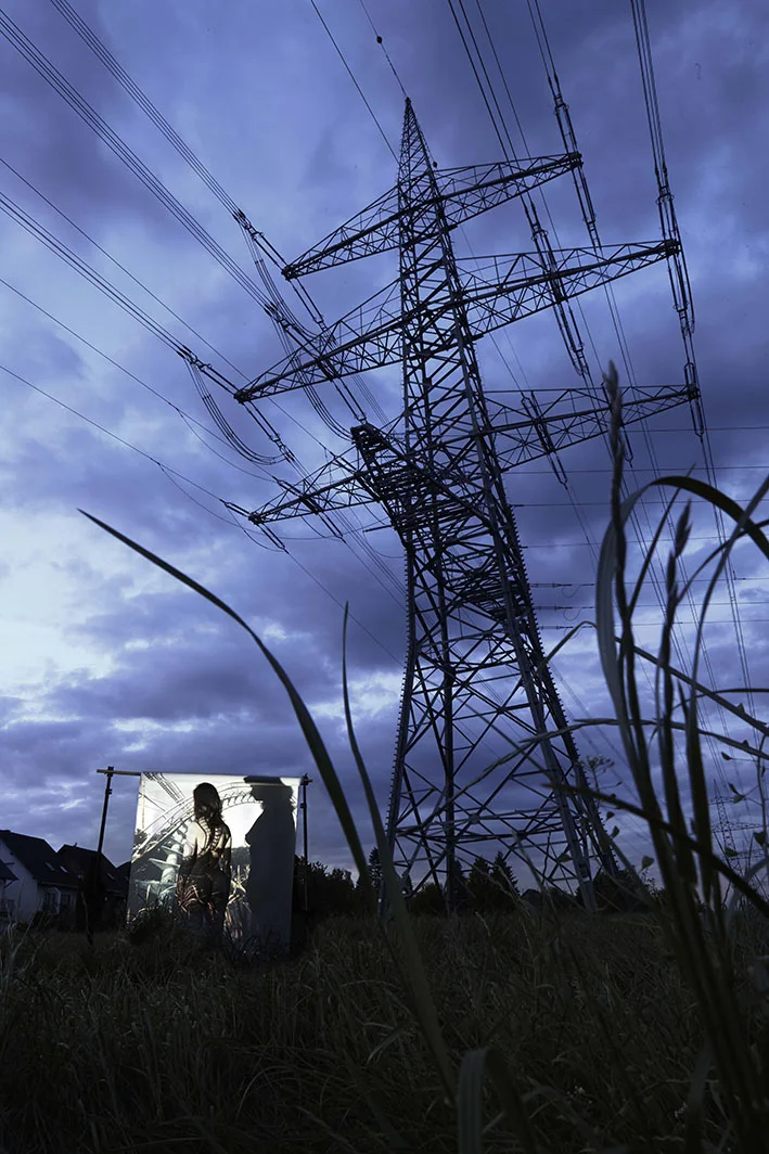 Projektion-Frau-steht-vor-angestrahlter-Leinwand-an-Strommast
