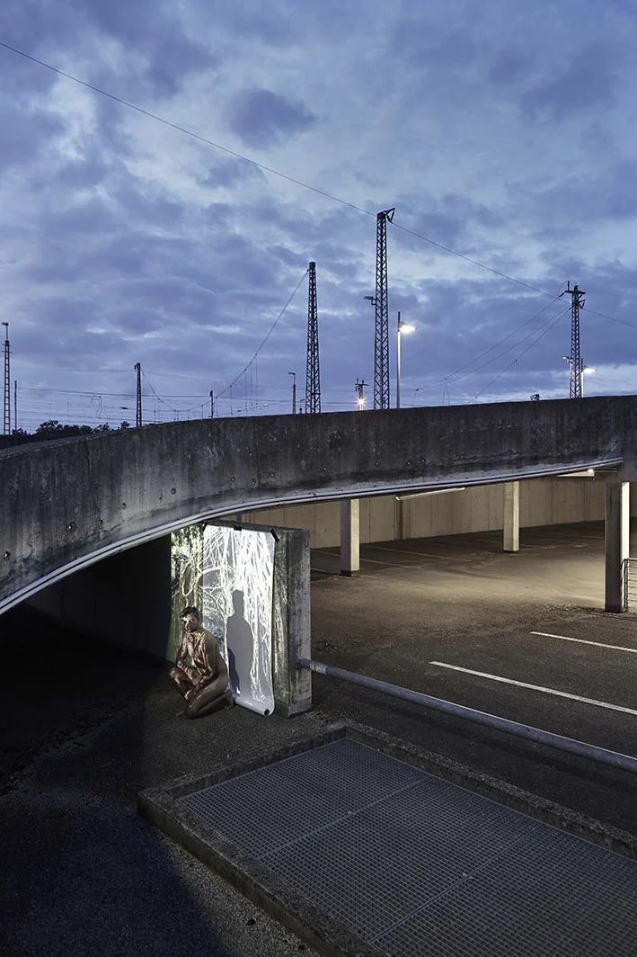 Projektion-Mann-kniet-vor-angestrahlter-Leinwand-auf-Parkplatz