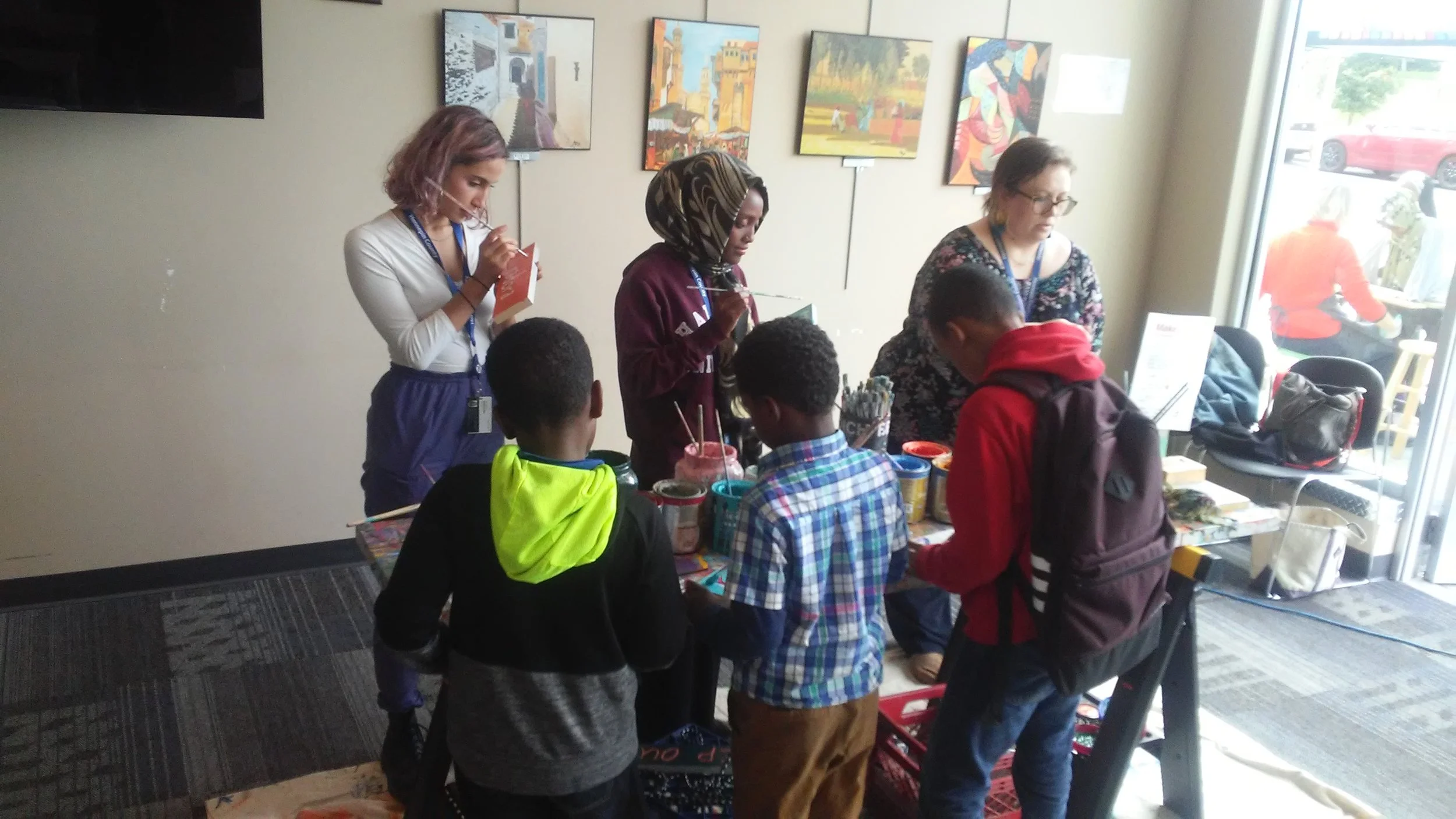 Teen Tech Squad members including Zubeda, center, along with community engagement librarian Sara Zettervall, right, help younger students with the afternoon's STEM-based project, sign painting with Springboard for the Arts.