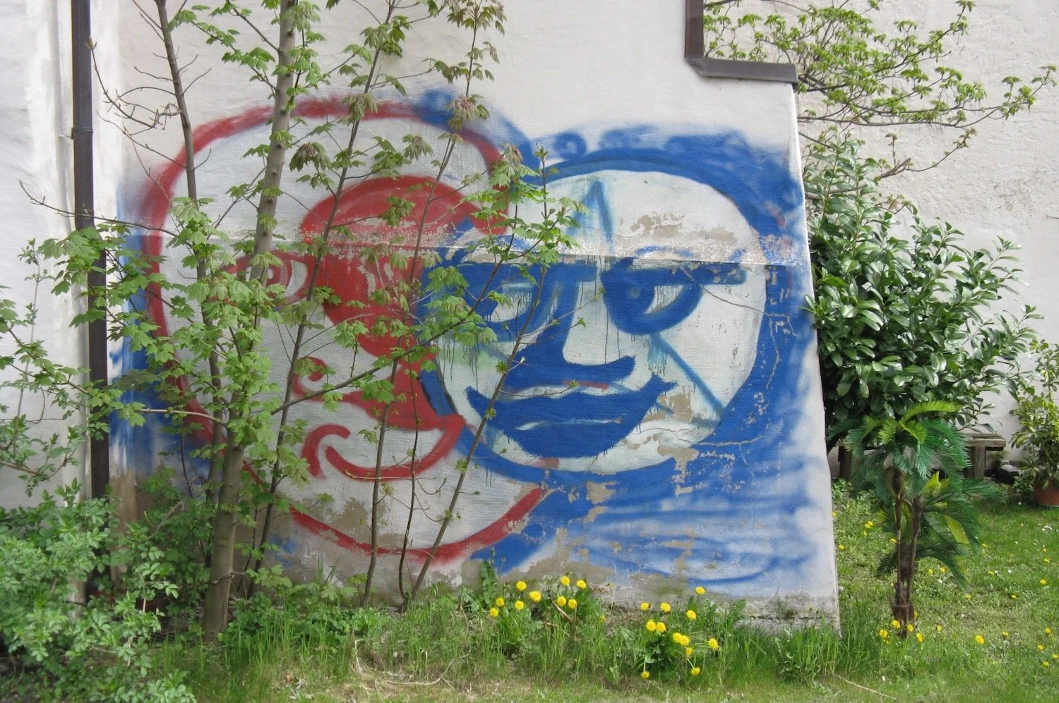 Graffiti on side of white building of a simple blue face smiling at a red face