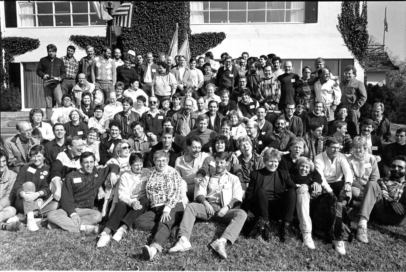 Dallas representatives clearly visible in this group photo: BJ Anderson (lower left corner, her hands around her right knee, wearing a dark sweater with white name tag), Mike Grossman (rear row, just right of center, wearing dark sweater with white shirt collar and white name tag), and John Thomas (third in from the upper right corner, standing behind the man in the white jacket).