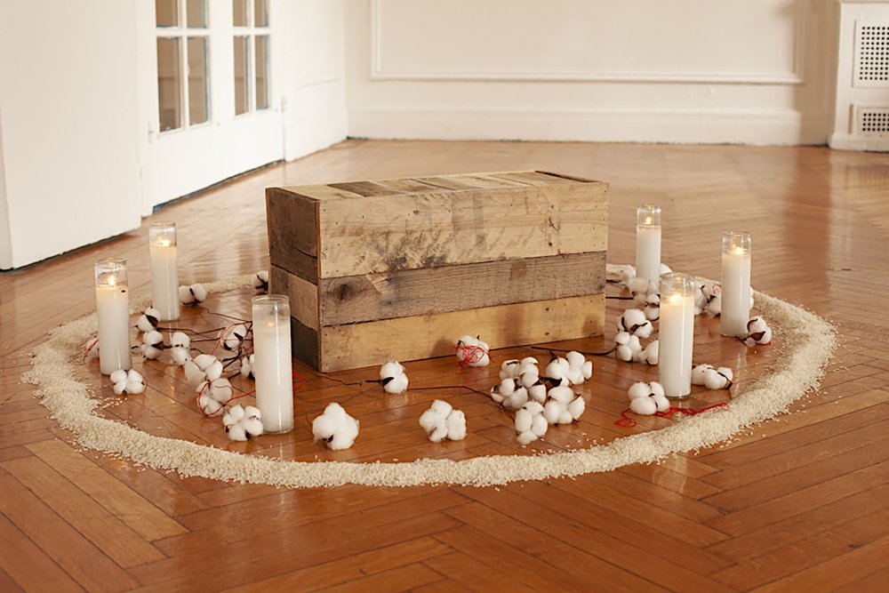   Auction Block , 2021, wooden crate, rice, cotton, candles, red thread, chalk, shells, 5’ circumference 
