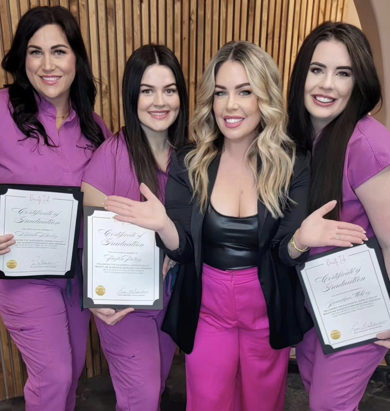 Women in pink scrubs holding certificates of graduation at a ceremony.