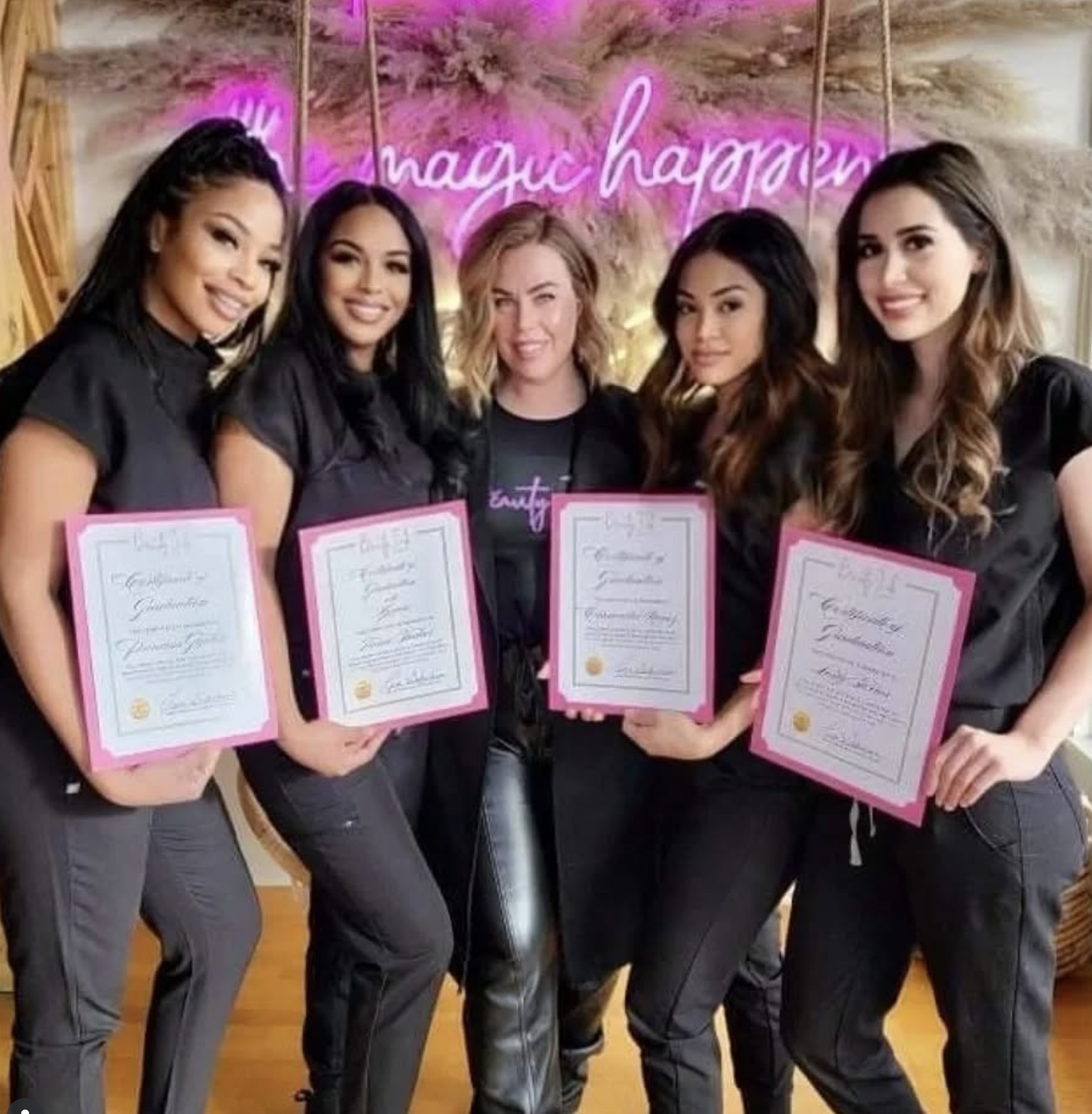 Five women standing side by side, holding certificates with pink borders, smiling at the camera, with a pink neon sign that says 'magic happy' in the background.