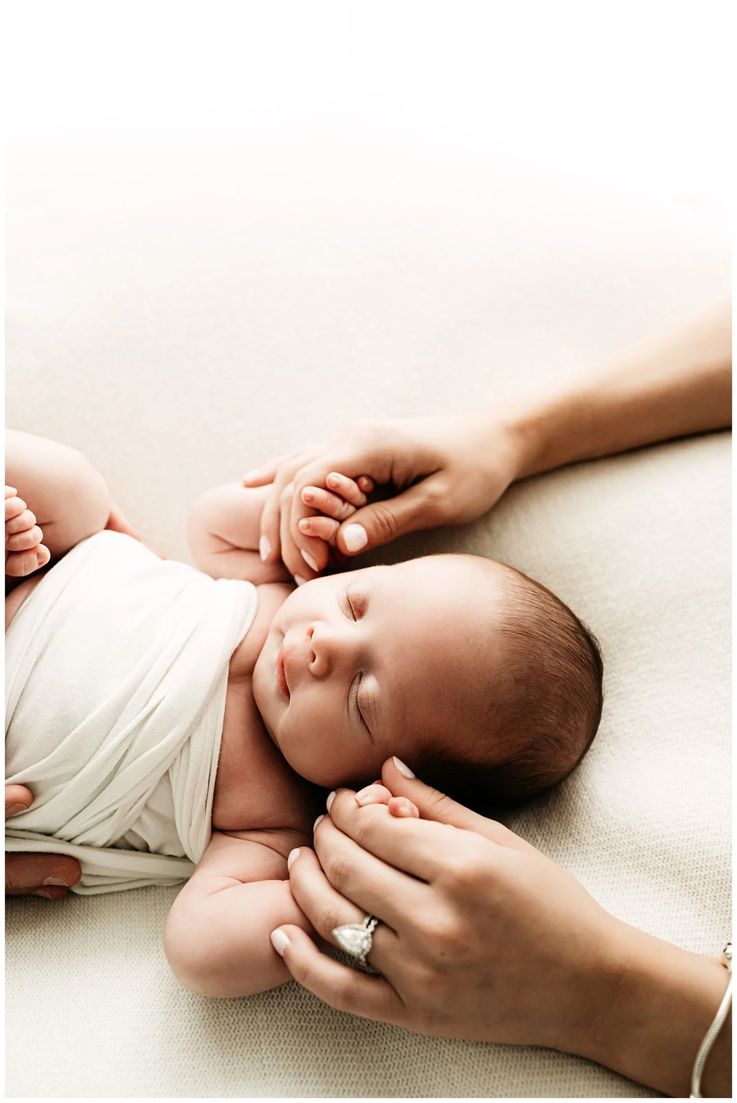 A photo depicting a mothers hands delicately holding her newborn baby's hands.