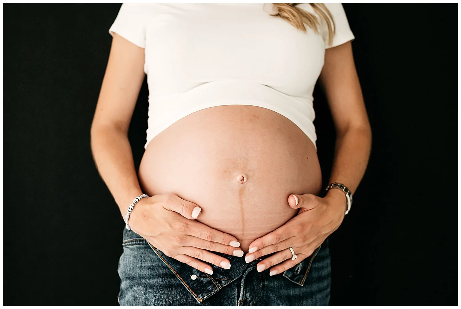 An up-close image of a mother's pregnant belly, with her hands cradling both sides.