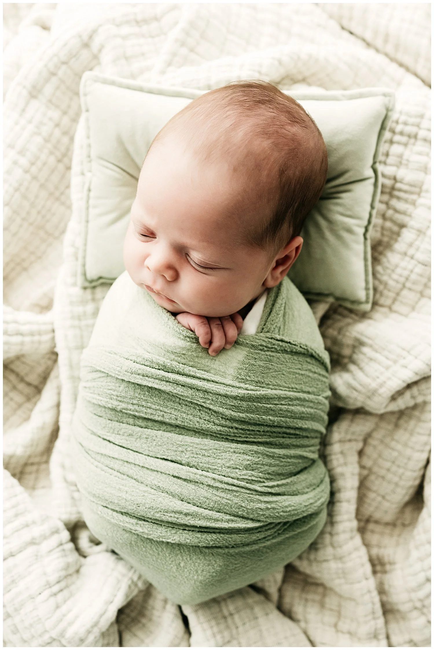 A photo of a sleeping baby swaddled in green wraps from a bird's eye view.