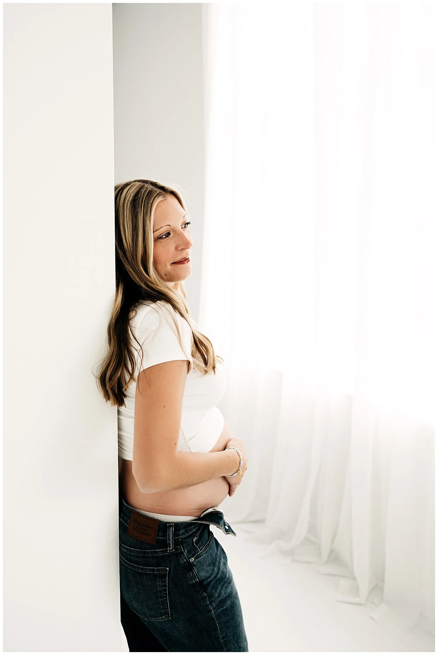 Expectant mom-to-be cradles belly while glancing out of the window before her.