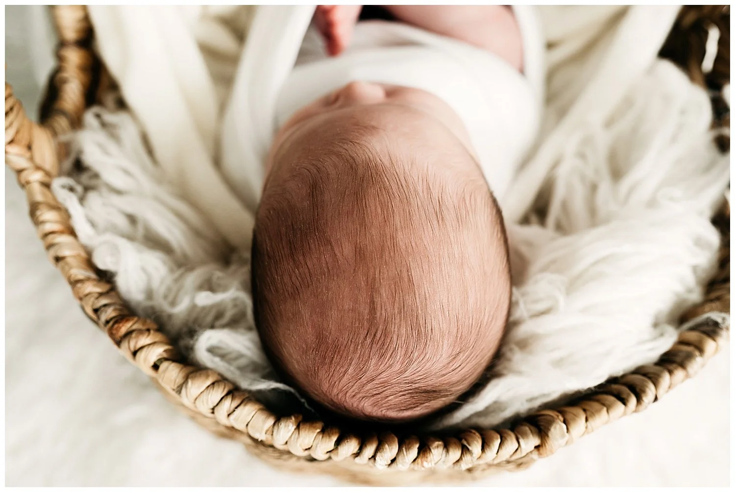 Close-up photo on a baby in a basket from a bird's eye view. The focus is on his wispy hairs.