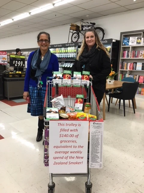 Miraka and Jo showing a trolley filled with $140 worth of groceries, equivalent to the average weekly spend of NZ smoker.