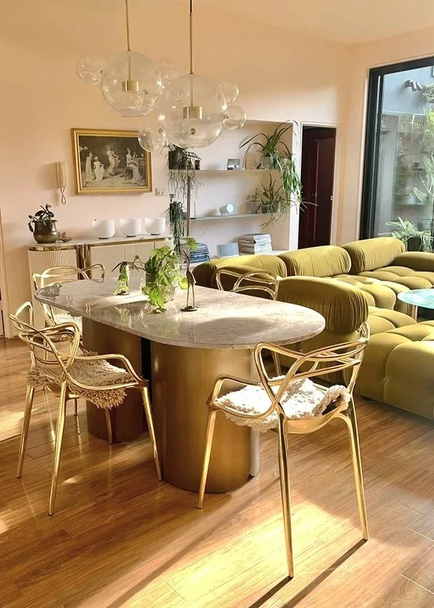Gwendolynne Burkin interior design project. Living room with a marble dining table, gold chairs with cushions, yellow sofa, bookshelf, wall art, hanging clear globe chandelier, and large glass sliding door with a garden view.