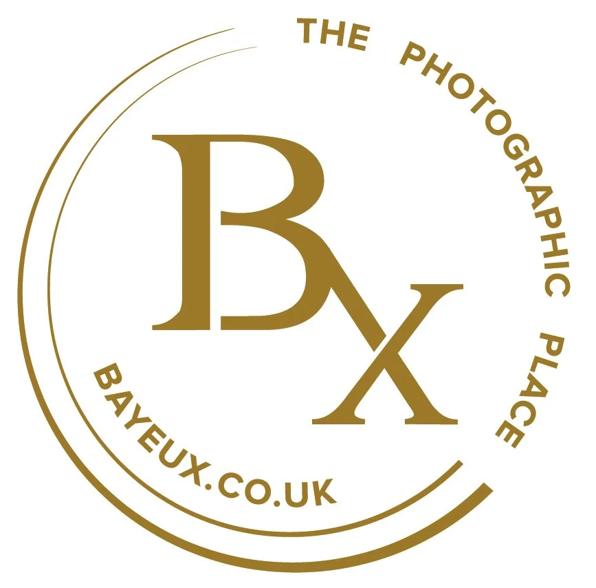 Logo of Bayeux, a photography company, with large initials 'B' and 'X' in the center, surrounded by the text 'The Photographic Place' at the top and 'bayeux.co.uk' at the bottom, all in gold color.