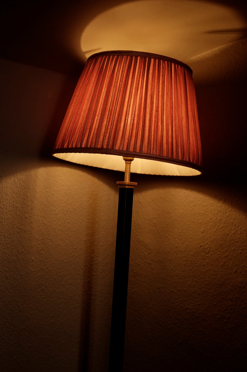 A floor lamp with an orange-striped fabric lampshade casting a warm glow on a beige wall.