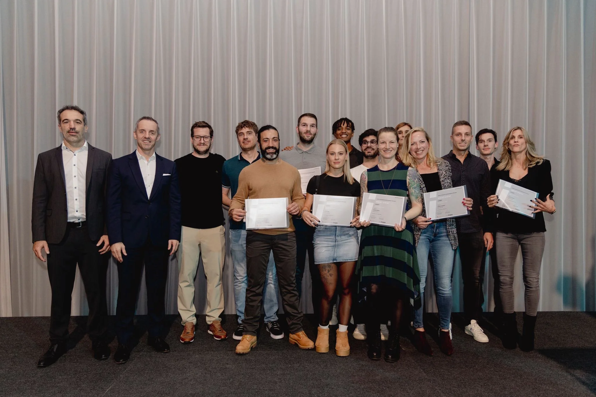 Group of people standing on stage, some holding certificates, at an awards or graduation ceremony.